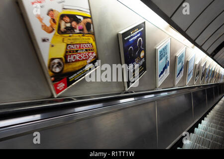 Ad posters on the wall next to an empty escalator on London Underground Tube Station Stock Photo