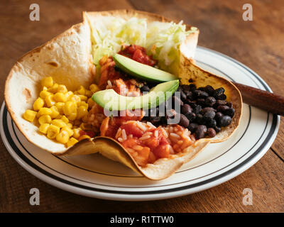 Mexican taco bowl with lettuce, corn, Mexican spicy, tomato rice, black beans, salsa and avocado on a flour tortilla. Stock Photo