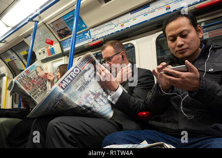 Tube commuters time, commuters reading and using smartphones and  london newspaper on the London Underground Tube Stock Photo