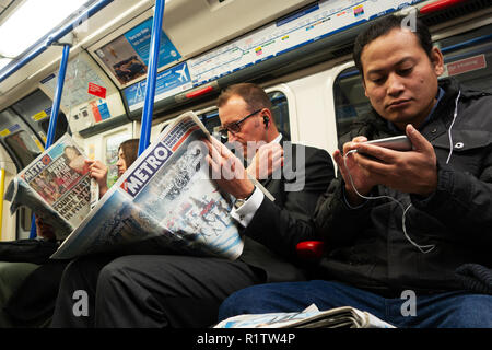Tube commuters time, Commuters reading and using smartphones and  london newspaper on the London Underground Tube Stock Photo