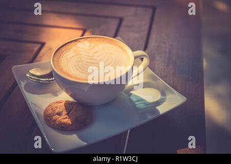 Beautiful morning wooden table top with coffee, latte art and cookie. Start the day, good mood concept. Stock Photo
