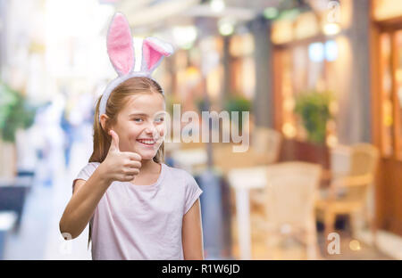 Young beautiful girl wearing easter bunny ears over isolated background doing happy thumbs up gesture with hand. Approving expression looking at the c Stock Photo