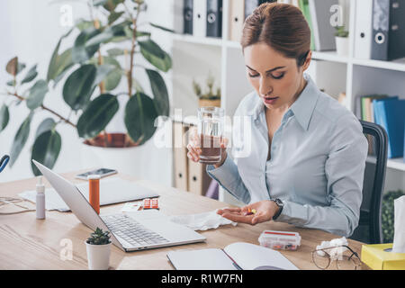 adult sick businesswoman taking pills at modern workplace Stock Photo