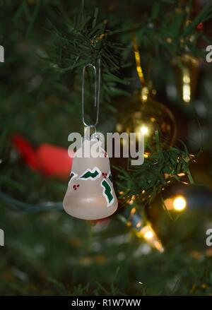 Holiday bell hanging on a Christmas tree with yellow tree lights in the background. Stock Photo
