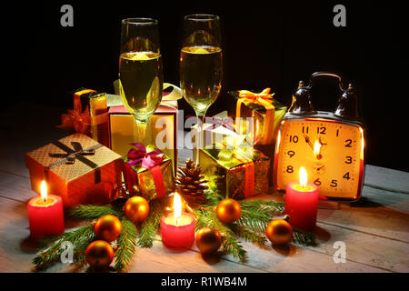 Glass of sparkling shampagne wine, clock, gift box and candles on christmas background. Stock Photo