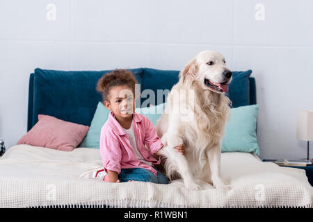cute african american kid sitting on the bed and holds dog paw Stock Photo