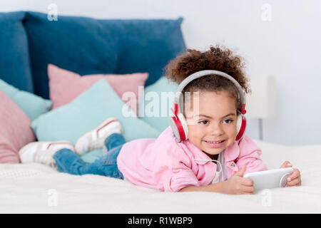smiling african american kid lying on the bed and listening music in headphones Stock Photo
