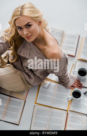 close up of woman sitting on open books with coffee cups isolated on grey