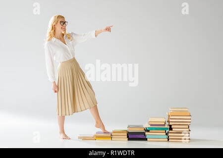 happy woman in glasses walking on steps made of books Stock Photo