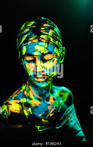 portrait of woman painted with bright neon paints on black backdrop Stock Photo