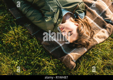 high angle view of beautiful young woman with closed eyes laying on blanket outdoors