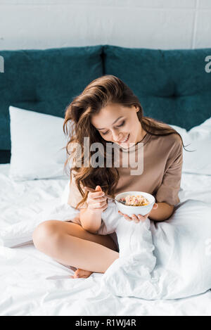 happy girl eating oatmeal for breakfast while sitting on bed Stock Photo