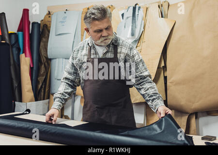 mature tailor in apron working with leather at workshop Stock Photo