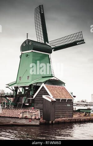 Windmill under cloudy sky on Zaan river coast, Zaanse Schans town, popular tourist attractions of the Netherlands. Suburb of Amsterdam Stock Photo