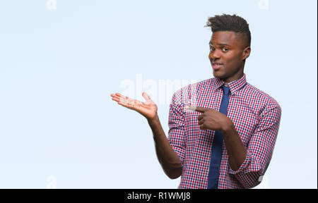 Young african american business man over isolated background amazed and smiling to the camera while presenting with hand and pointing with finger. Stock Photo