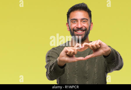 Adult hispanic man wearing winter sweater over isolated background smiling in love showing heart symbol and shape with hands. Romantic concept. Stock Photo