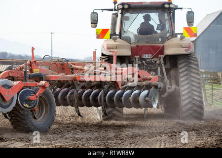 A red tractor and plough working to prepare a field for sowing in Canterbury, New Zealand Stock Photo