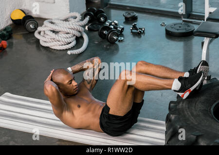 tattooed african american athlete doing abs with legs on tire at gym Stock Photo