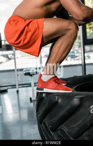 cropped image of african american athlete exercising on tire at gym Stock Photo