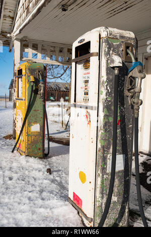 Closed gas station in rural west with weathered wood white building and 2 50's style pumps and snow on the ground