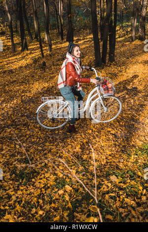 high angle view of girl in leather jacket and beret riding on bicycle in yellow autumnal forest Stock Photo