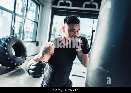 young sportsman wearing boxing gloves and punching boxing bag at gym