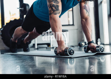 cropped view of young sportsman doing push ups with dumbbells in gym on sport mat Stock Photo