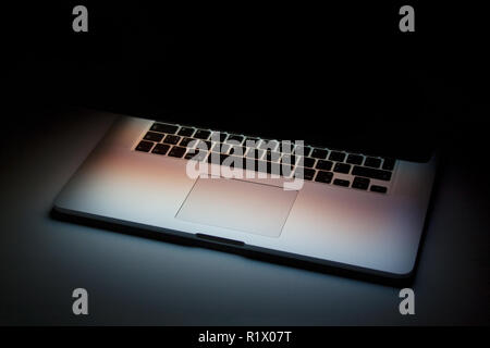 Half closed silver laptop with screen light isolated on dark background Stock Photo