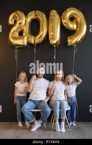 Happy family holding sign 2019 made of golden balloons for new year on black background. Stock Photo