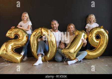 Happy family holding sign 2019 made of golden balloons for new year on black background. Stock Photo