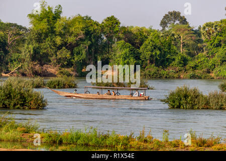 Don Det, Laos - April 22, 2018: Wooden boat navigating the mekong river surrounded by forest near the Cambodian border Stock Photo