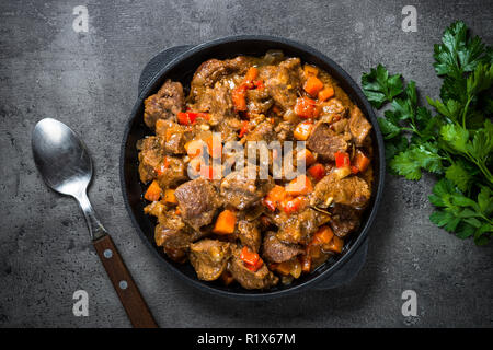 Beef stew with vegetables in iron pan on black. Stock Photo