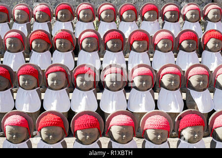 row of buddhist mizuko jizo statues with red bib, hat Stock Photo