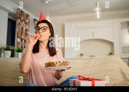 A girl in a cap alone with a cake with candles in the room. Stock Photo