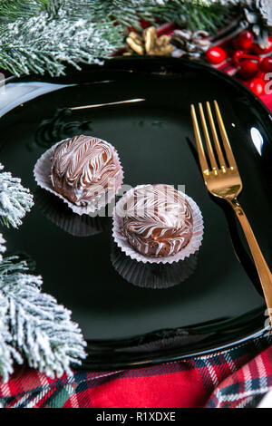 Delicious dark chocolate cakes covered with glazed. Tasty dessert food in close up. Chocolate desserts served on black plate, decorated fir branches.  Stock Photo