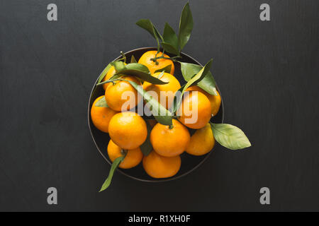 Fresh mandarins with leaves in bowl on black. Healthy eating concept. Copy space. Stock Photo