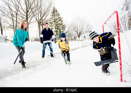 A Happy funny kids playing hockey with father on street in the winter season Stock Photo