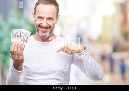 Senior hoary man holding buch of dollars over isolated background with surprise face pointing finger to himself Stock Photo