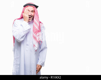 Senior arab man wearing keffiyeh over isolated background covering one eye with hand with confident smile on face and surprise emotion. Stock Photo