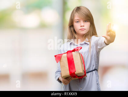 Young blonde toddler holding a present with open hand doing stop sign with serious and confident expression, defense gesture Stock Photo