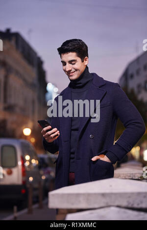night time sunset, one young man, 20-29 years old, standing looking to smartphone. wearing Autumn clothes. Stock Photo