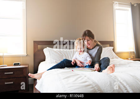 A Cute little girl reading a book with her mother in the bedroom Stock Photo