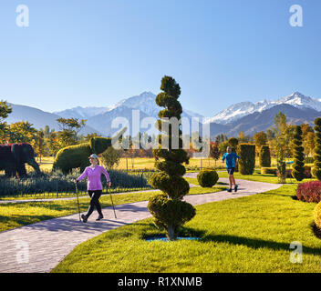 Young couple training in topiary park. Man is jogging and woman doing Nordic walking with poles. Healthy life concept. Stock Photo