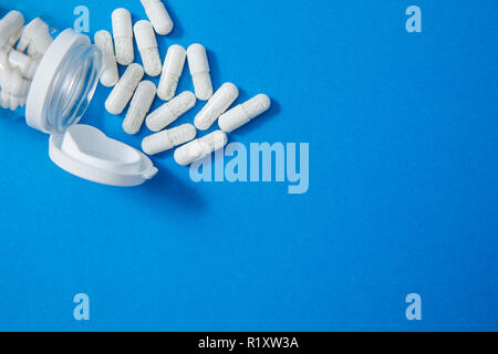 Spilled pills and jar on blue background with copyspace on right side Stock Photo