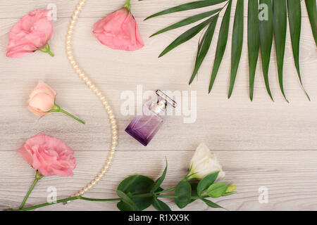 Bottle of perfume, beads on a string with white and pink flowers and green leaves on wooden background. Woomen cosmetics. Top view. Stock Photo