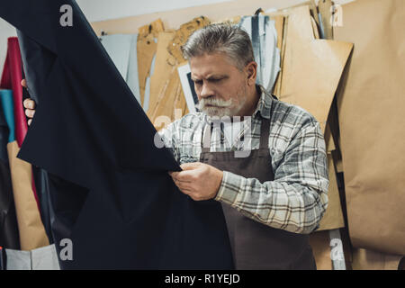 concentrated handbag craftsman looking at leather in workshop Stock Photo