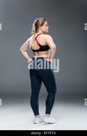 back view of young overweight woman in sportswear standing with hands on waist on grey Stock Photo
