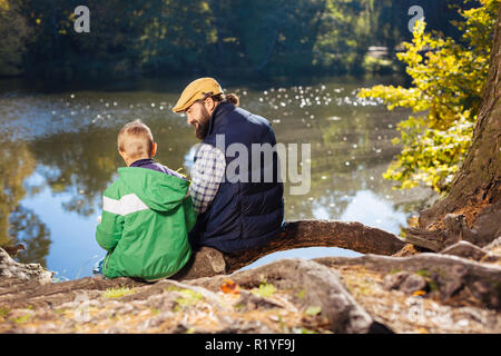 Nice positive man and boy sitting on the tree root Stock Photo