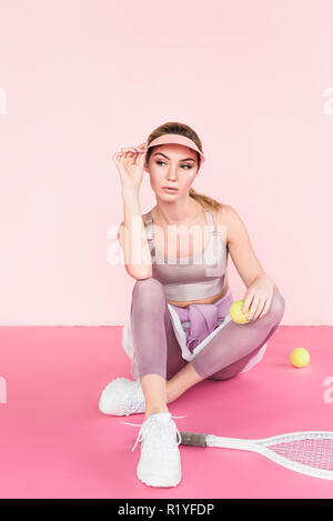 beautiful female athlete in visor hat posing with tennis racket and balls on pink Stock Photo