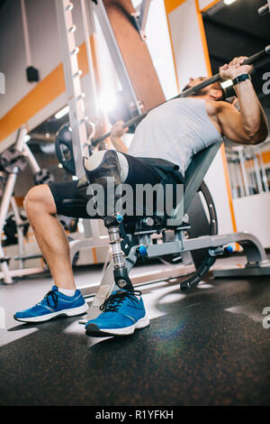 athletic young sportsman with artificial leg lifting barbell at gym Stock Photo